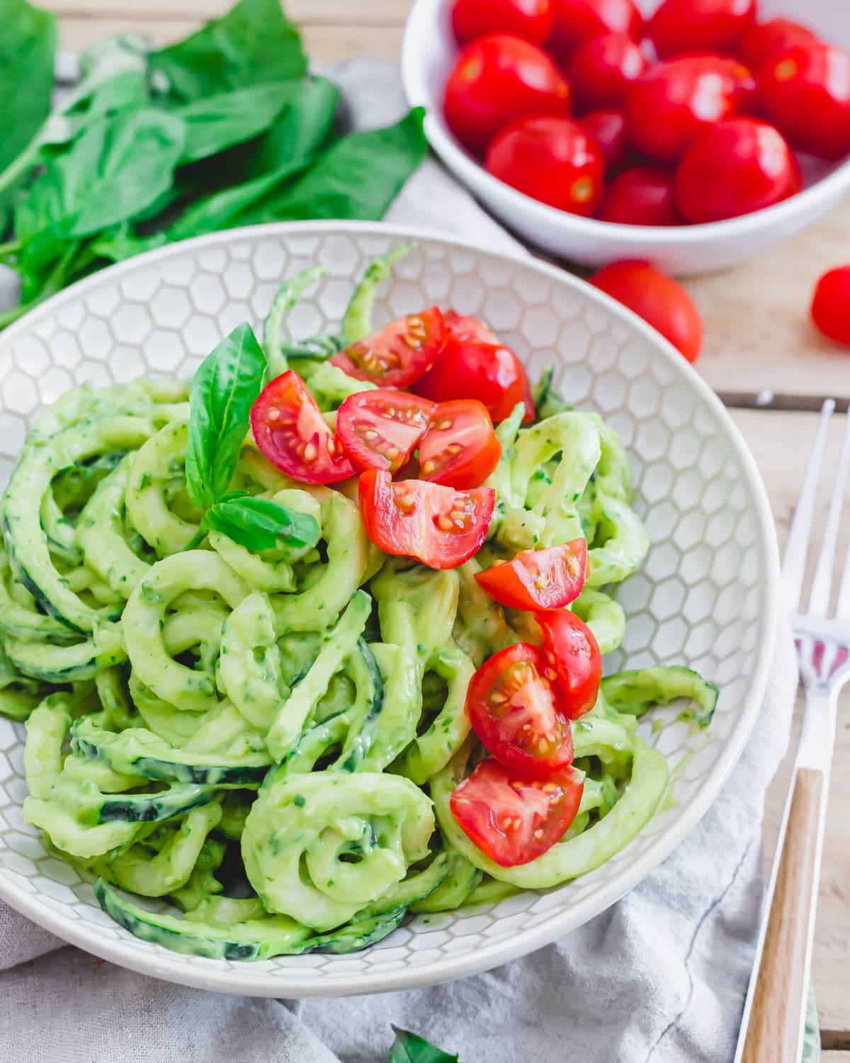 Zucchini noodles with pesto and tomatoes in a white bowl.