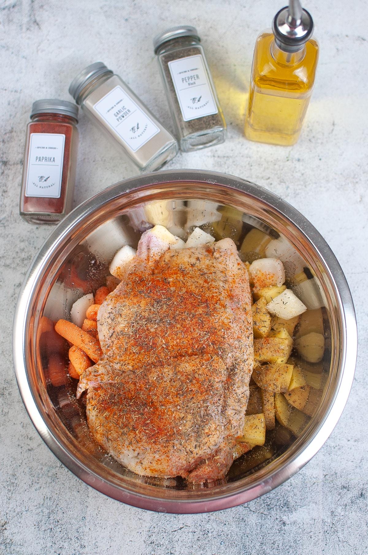 Half chicken, vegetables, and spices in a mixing bowl.