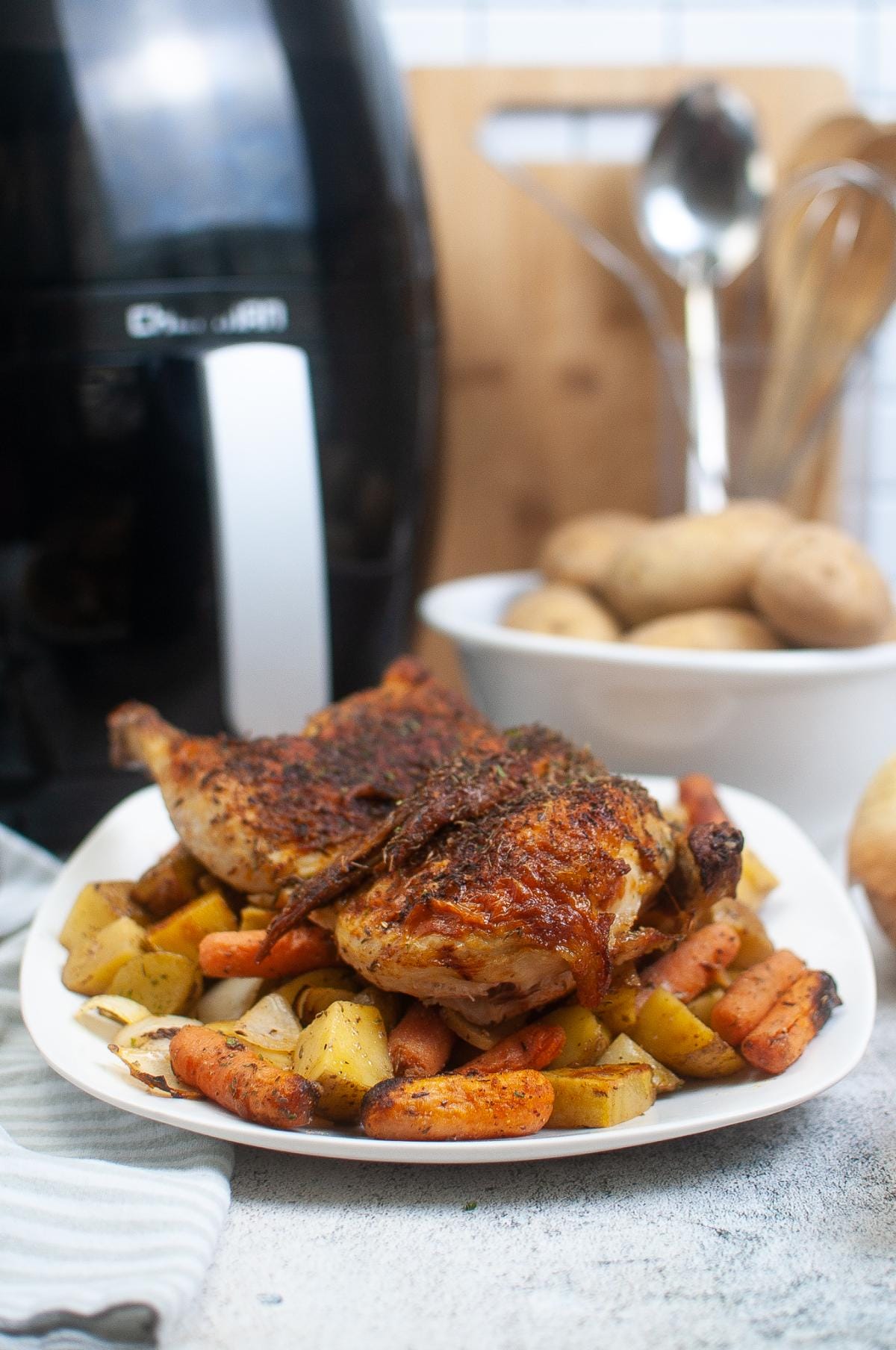 A plate with cooked half chicken and vegetables next to an air fryer.