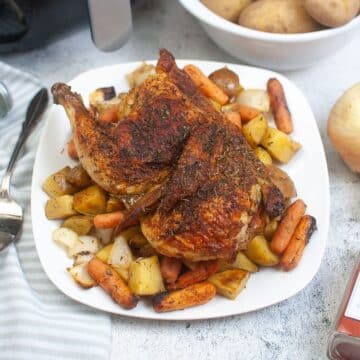 Air fried half chicken with roasted potatoes and carrots on a plate.