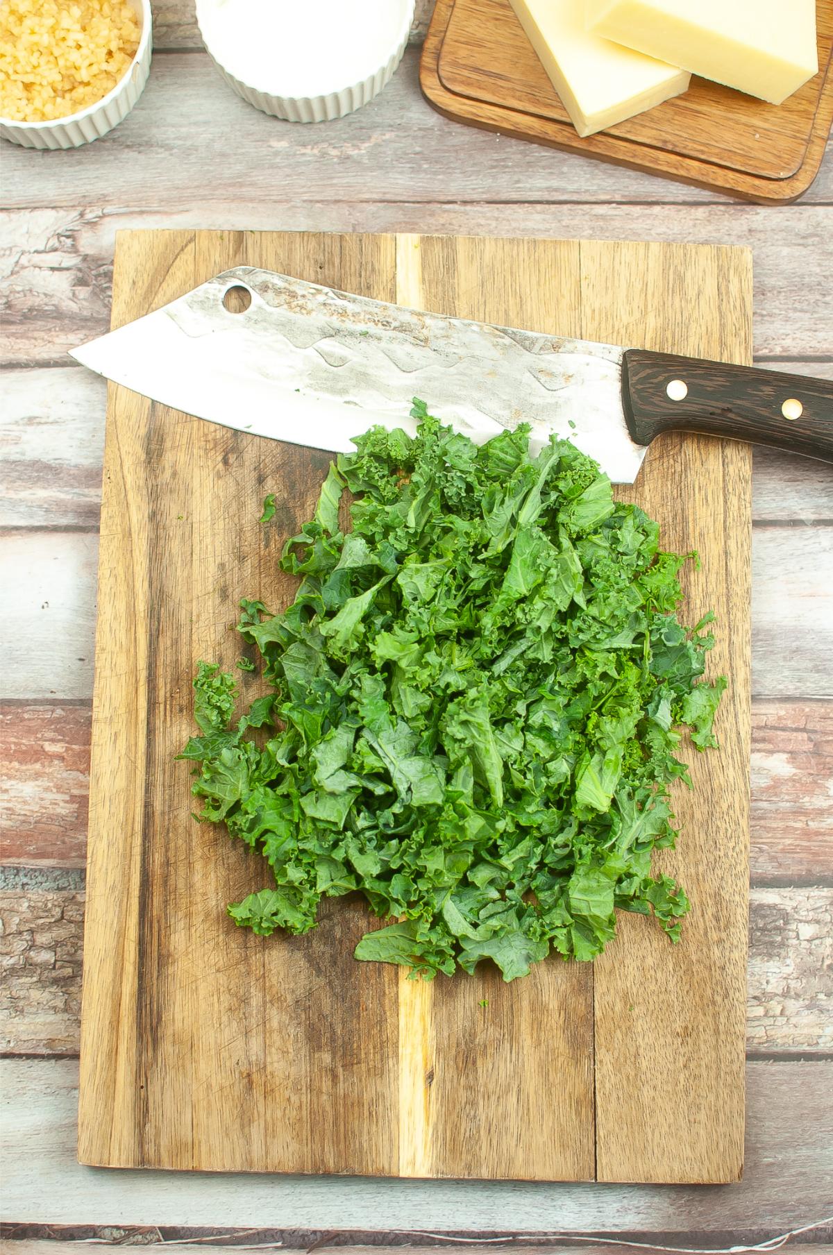 A cutting board with chopped kale leaves and big knife.