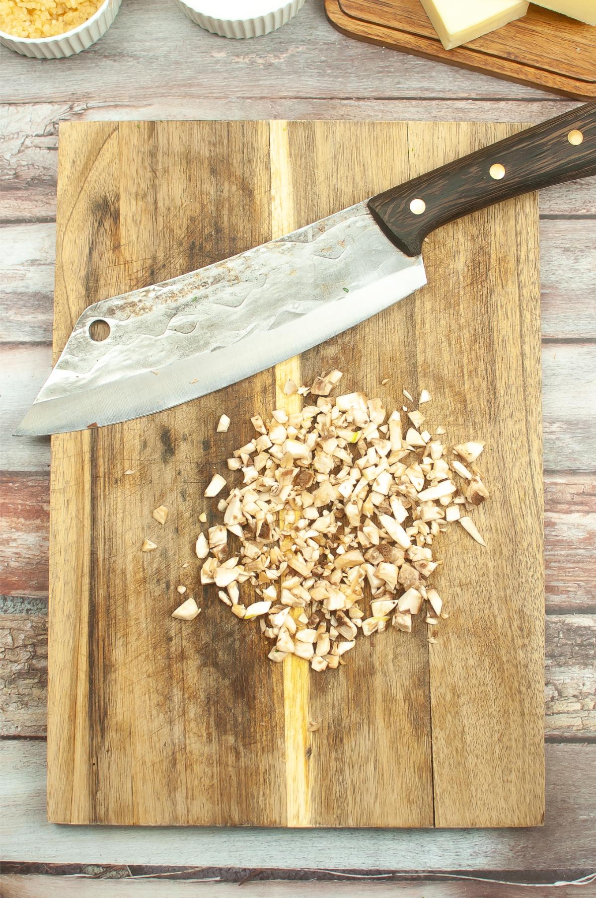 A cutting board with chopped mushrooms and big knife.