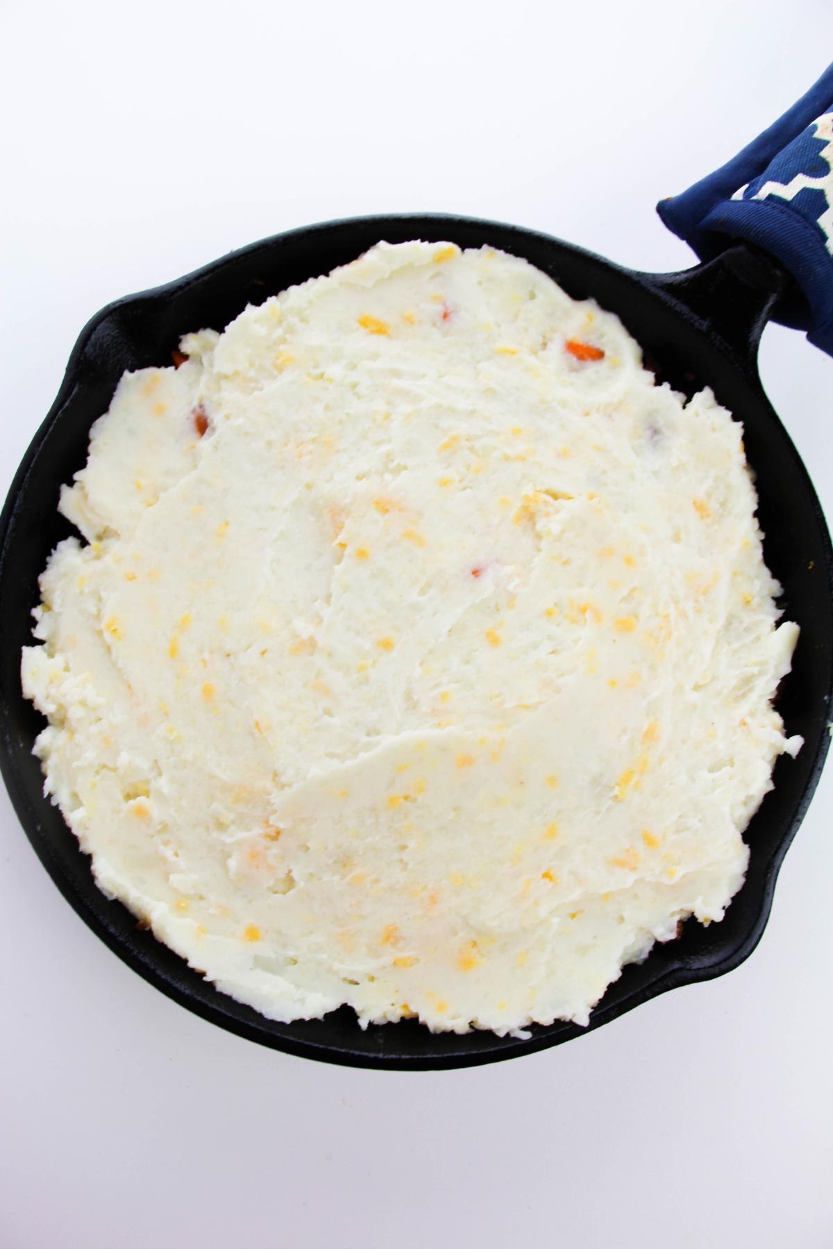 Mashed potato over the meat and vegetable filling in a cast iron skillet.