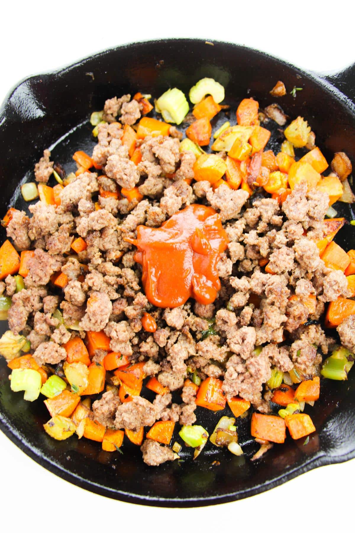 Cooked mixed vegetables, ground beef and tomato paste in cast iron skillet.