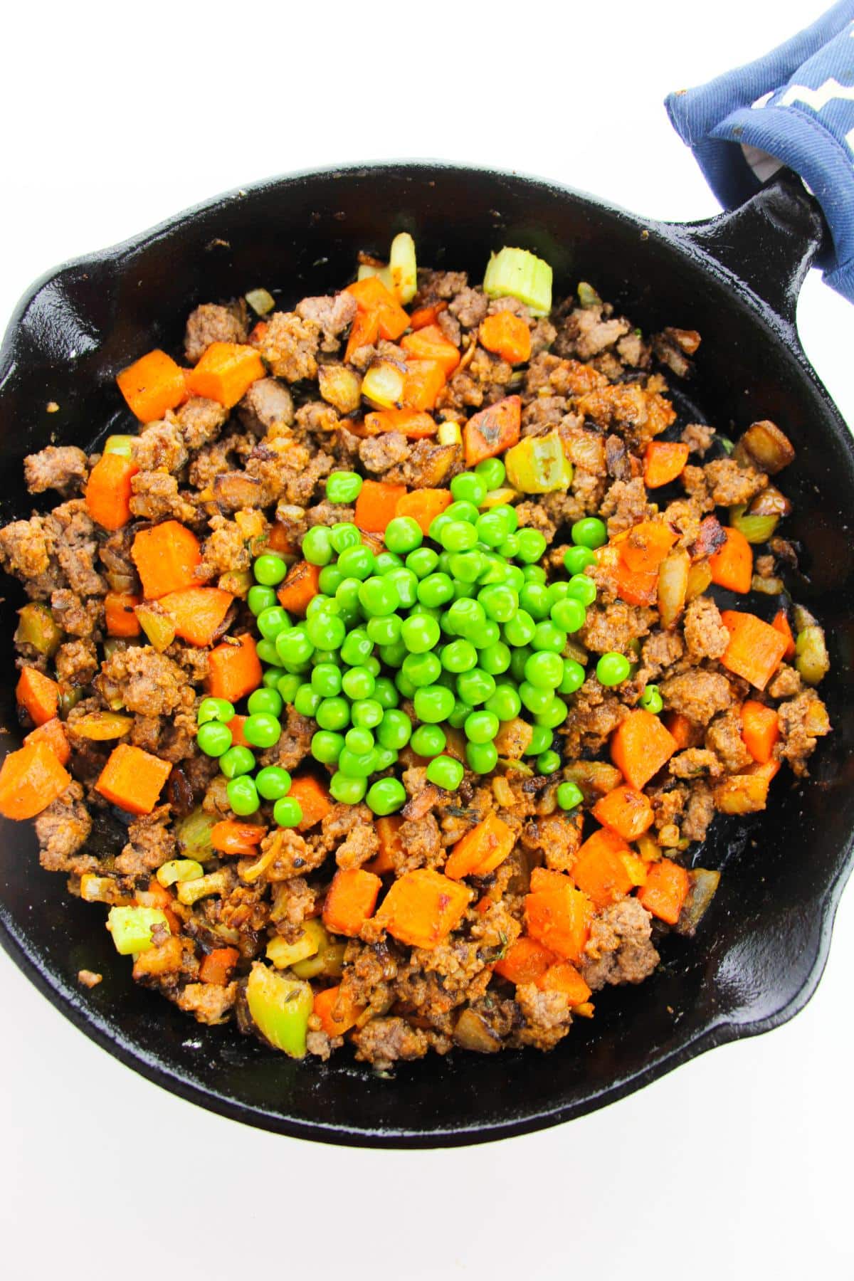 Cooked mixed vegetables, ground beef and green peas in cast iron skillet.