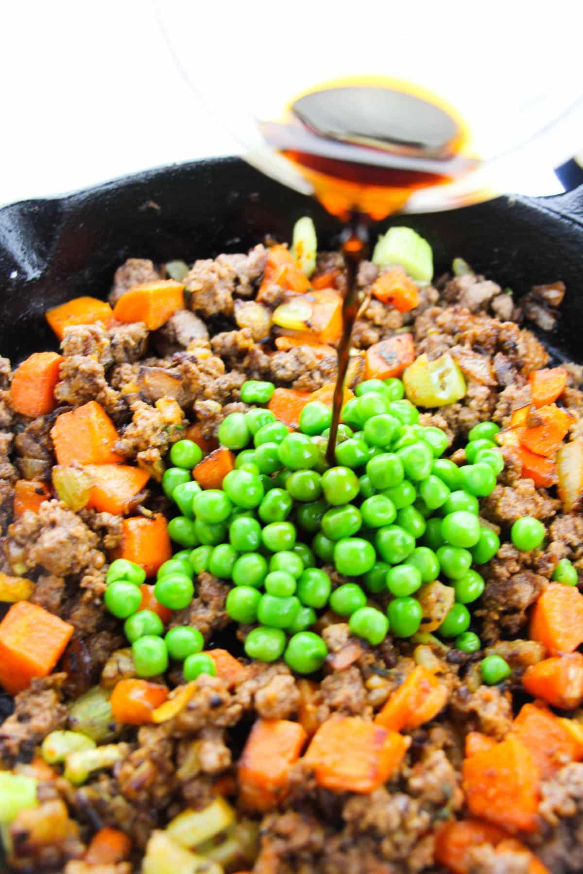Worcestershire sauce is being poured in the mixed vegetables and ground beef mixture.