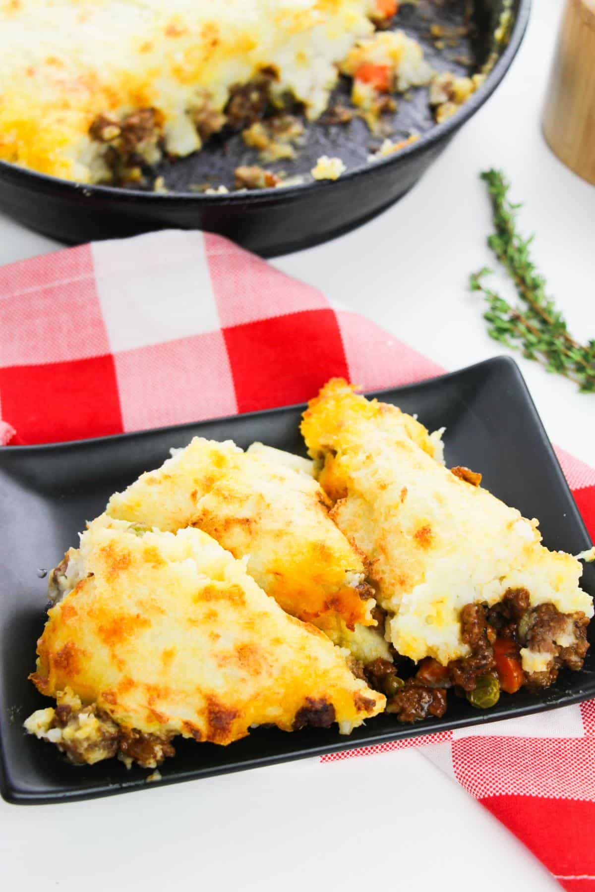 A plate of Cast Iron Shepherd's Pie on a table with a red and white checkered table cloth.