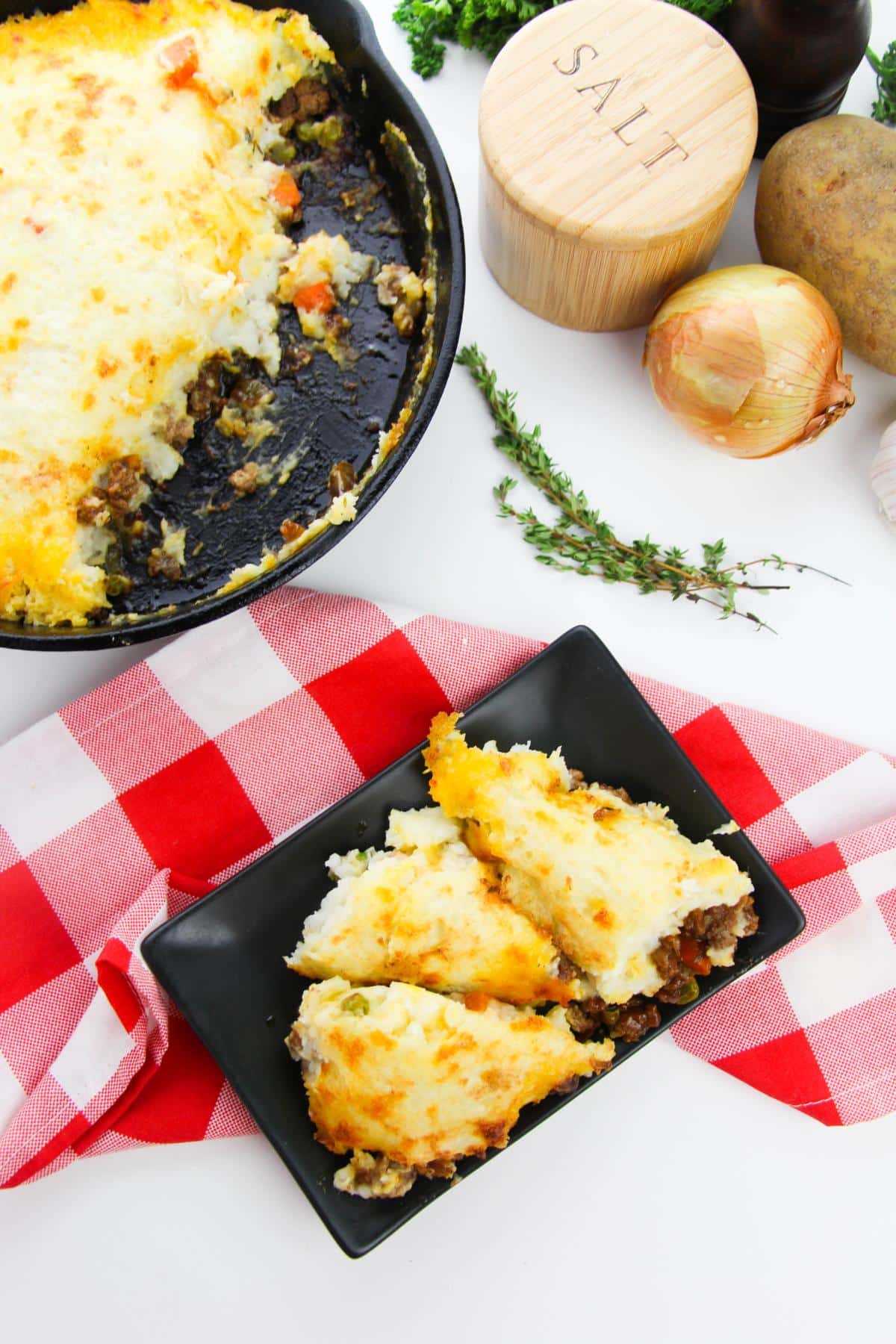 Overhead view of Cast Iron Shepherd's Pie on a black plate on a red and white checkered tablecloth.