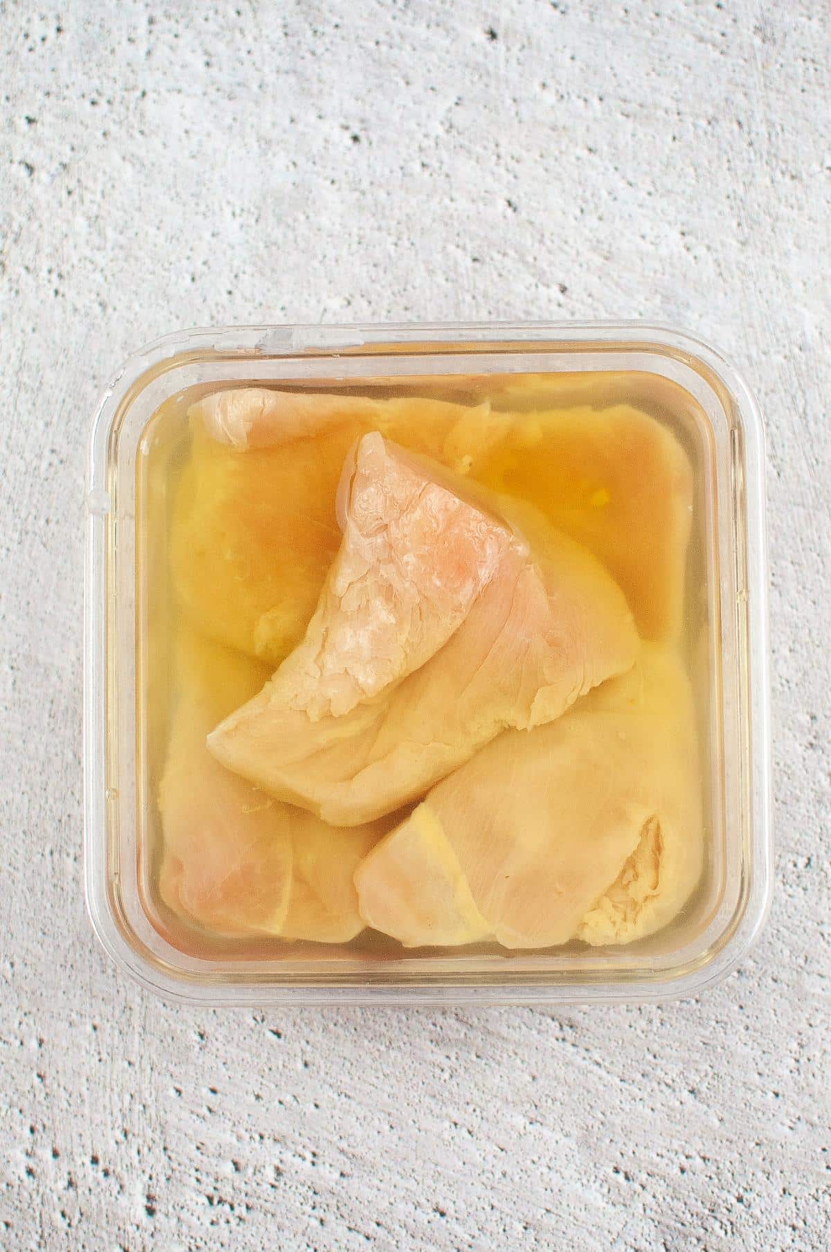 A glass bowl, which is filled with pickle juice and water, is used to marinate chicken breasts.