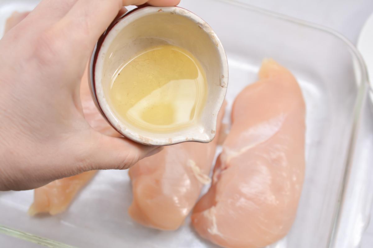 Person is pouring olive oil onto chicken breasts in a baking dish, for chicken cordon bleu.