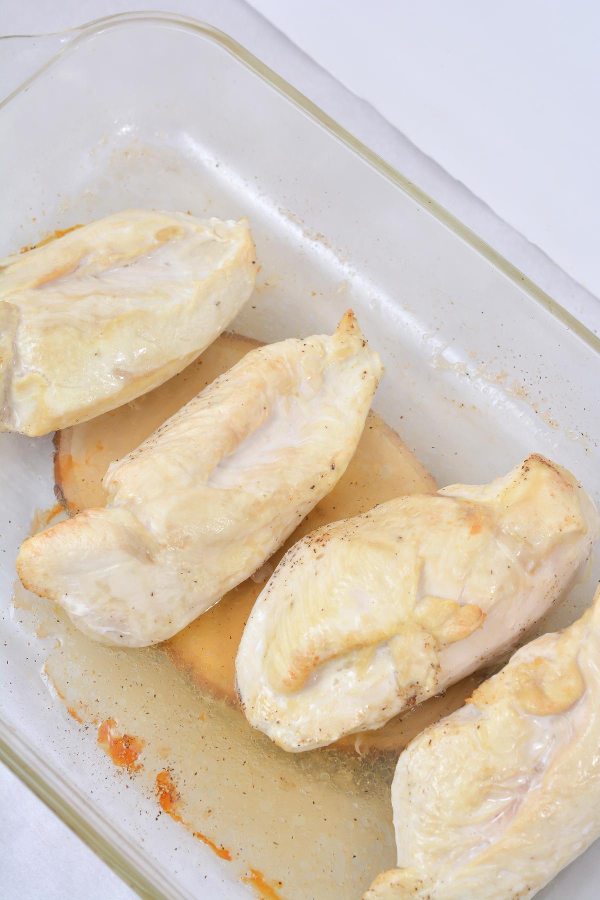 Four pieces of chicken breast in a baking dish