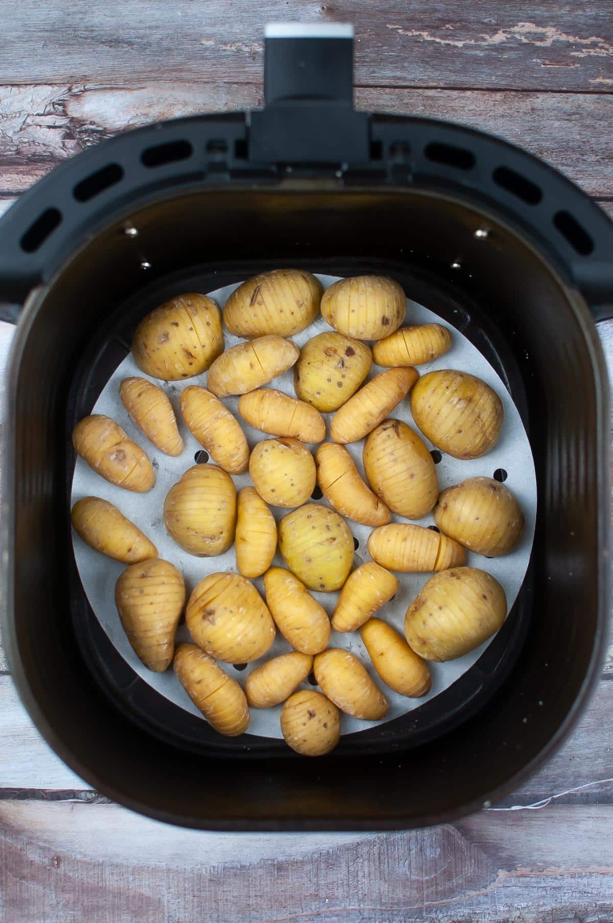 Potatoes inside the Air fryer on a wooden table.