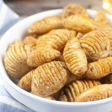 A bowl full of fried hasselback potatoes on a table next to a bottle of wine.