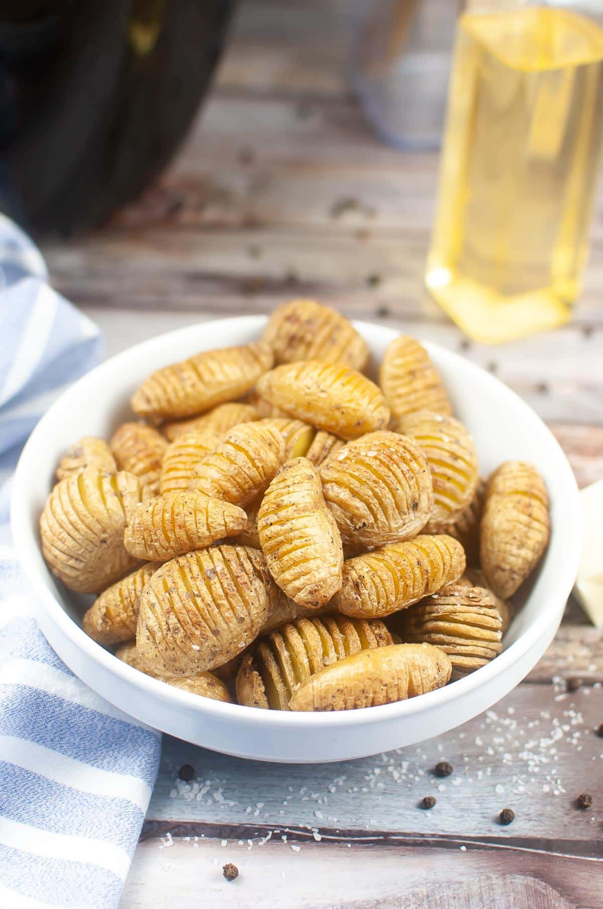 A bowl full of Hasselback potatoes on a table next to a bottle of olive oil.