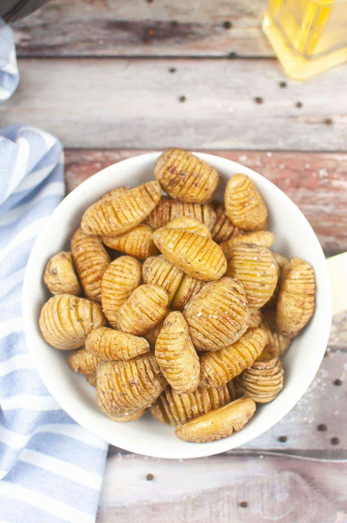 Hasselback potatoes in a white bowl on a wooden table.