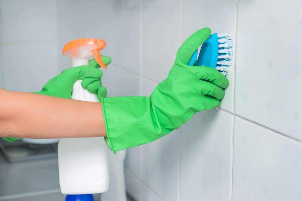 Using vinegar, a person in green gloves effortlessly cleans the tile grout.