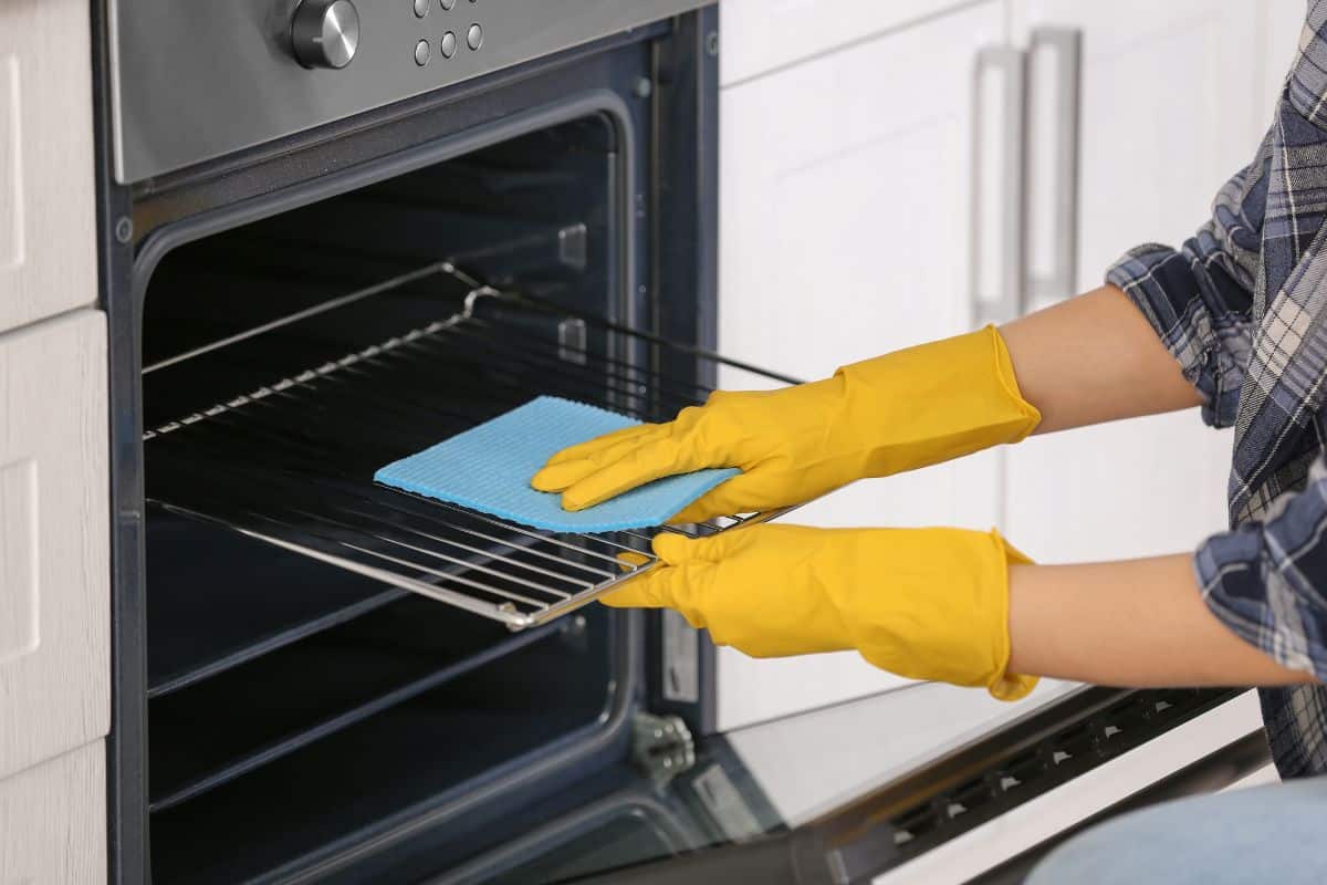A woman in yellow gloves cleaning an oven rack using clean cloth.