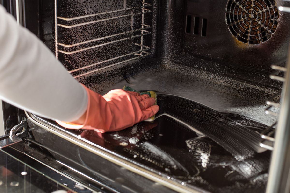 A woman using a baking soda paste to clean the oven.