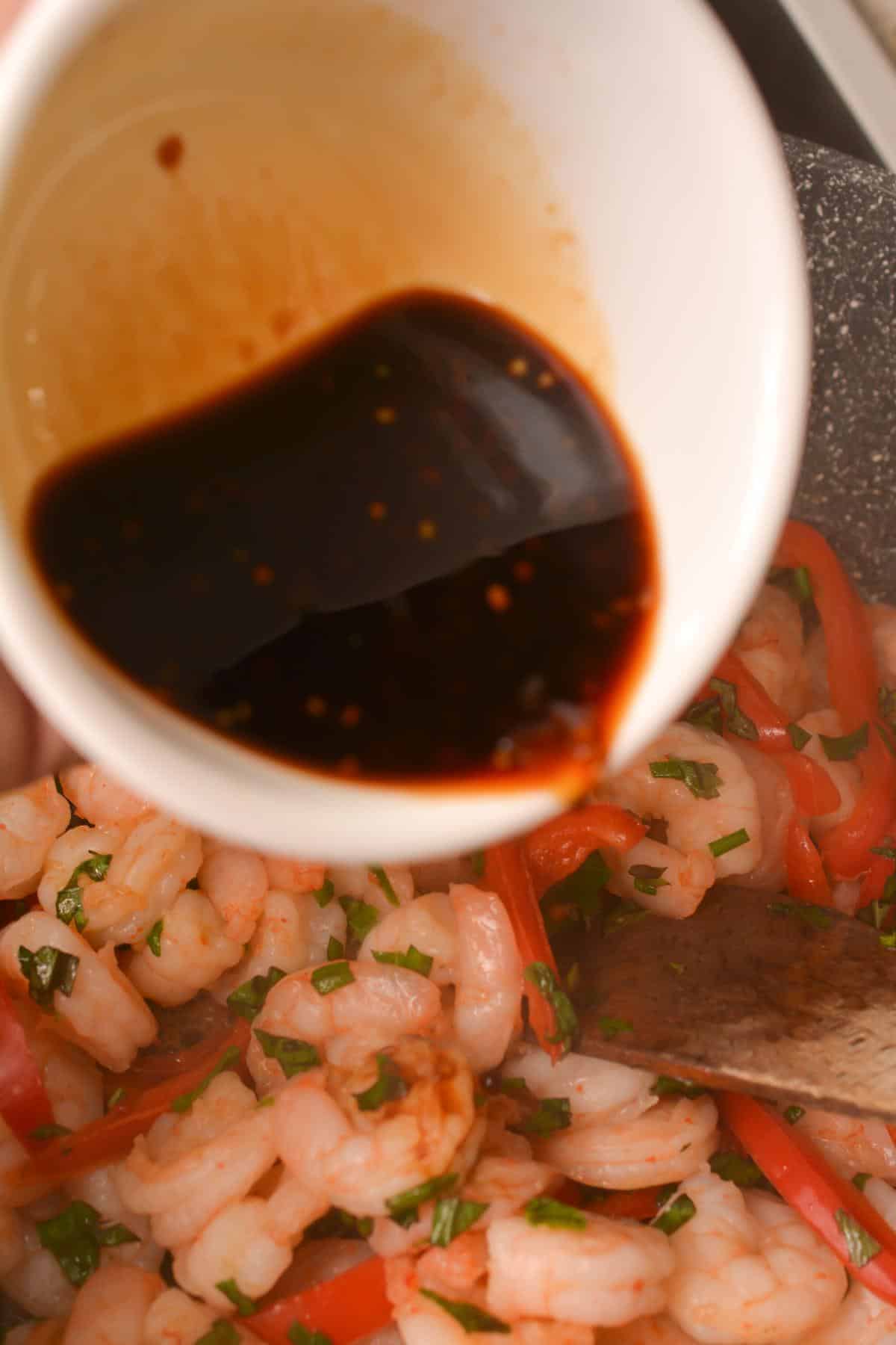 A person is pouring sauce over shrimp in a pan.