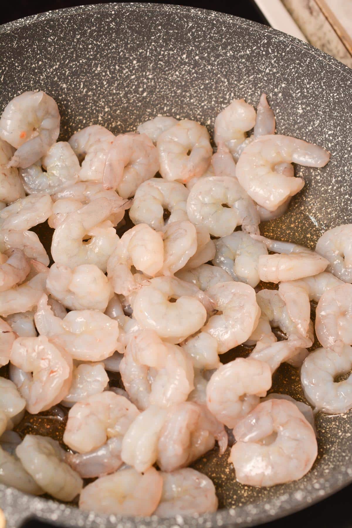 Shrimp being cooked in a frying pan on top of a stove.