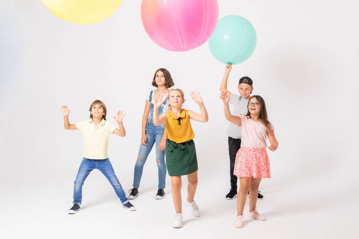 A group of children playing minute to win it games while tossing balloons.