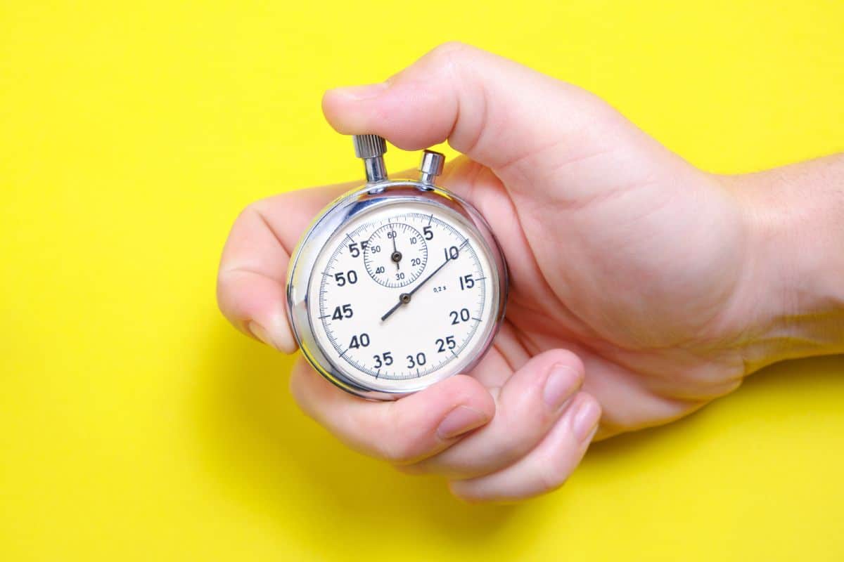 A man's hand holding a stopwatch on a yellow background.