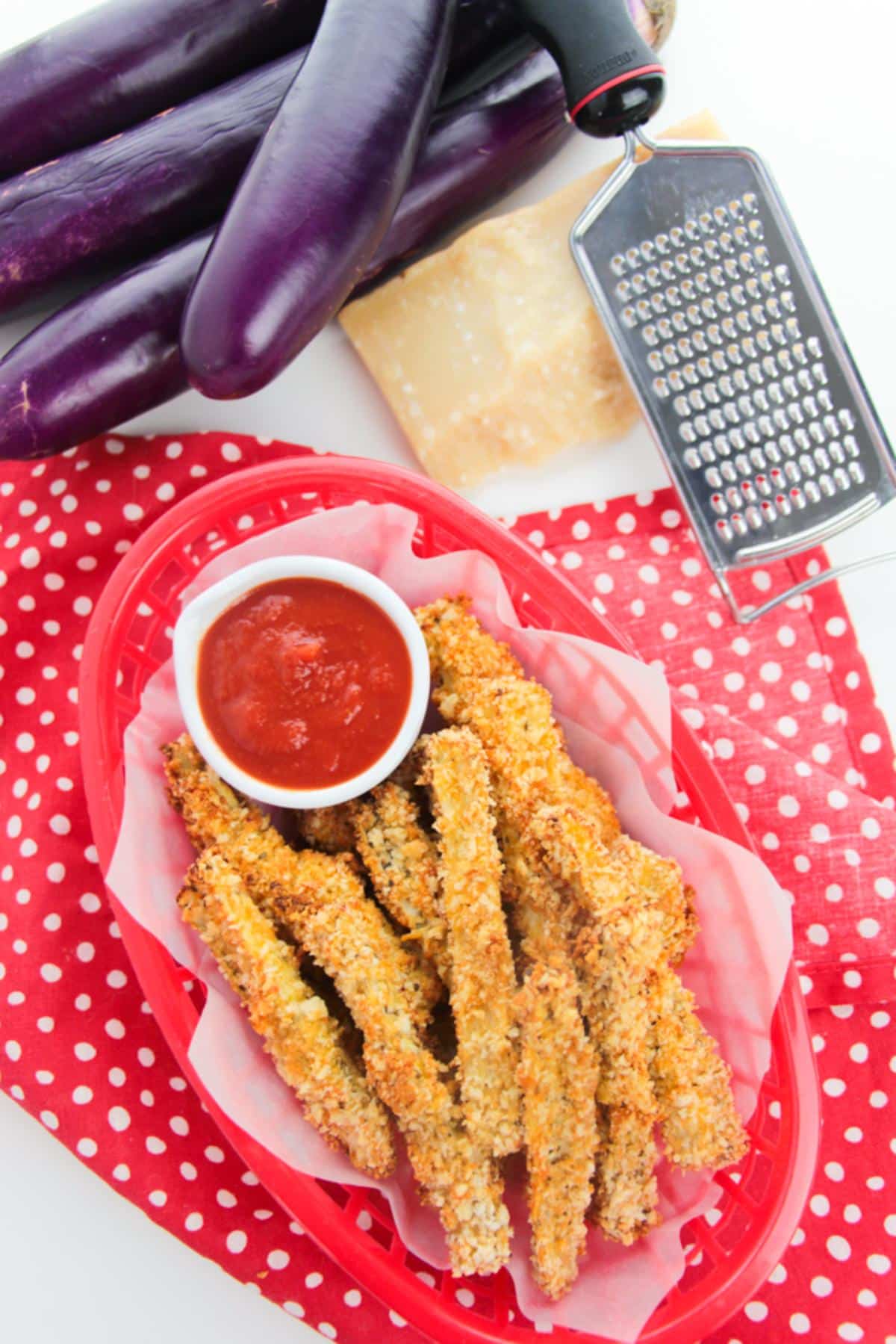 Overhead view of Panko eggplant fries on a red plate with dipping sauce on a red polka dot tablecloth.