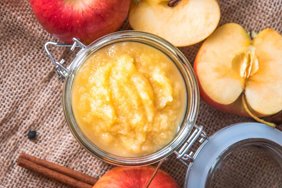 Applesauce in a jar with apples and cinnamon on the side.