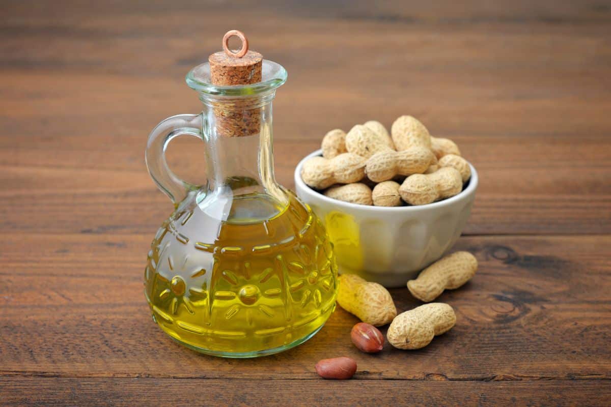 Peanut oil in a bottle and peanuts in a white bowl on a wooden table.