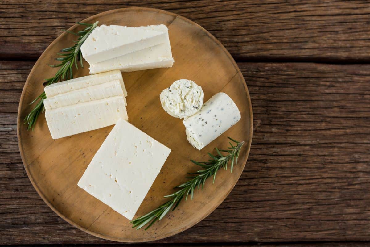 Various goat cheese on wooden plate, on a wooden table with Rosemary sprigs on the side.