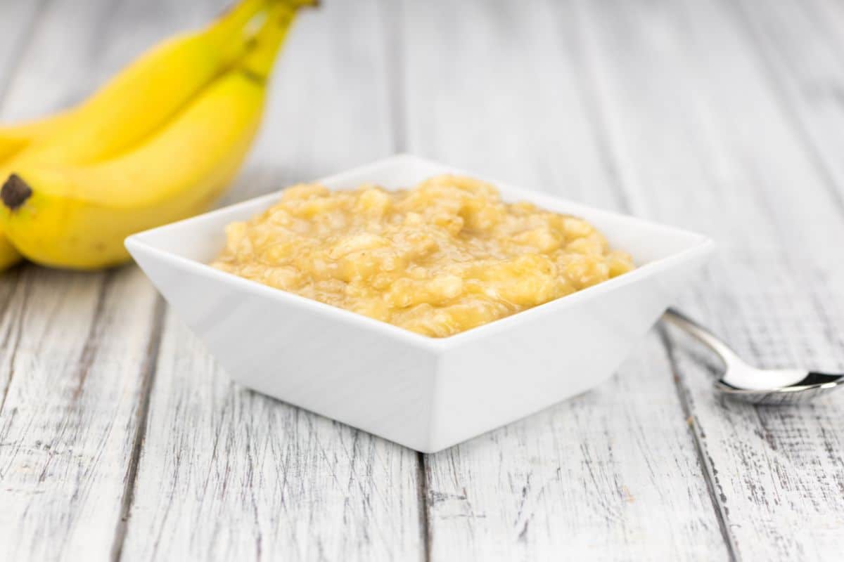 A bowl of mashed banana and spoon on a wooden table, perfect for Greek yogurt substitutes.
