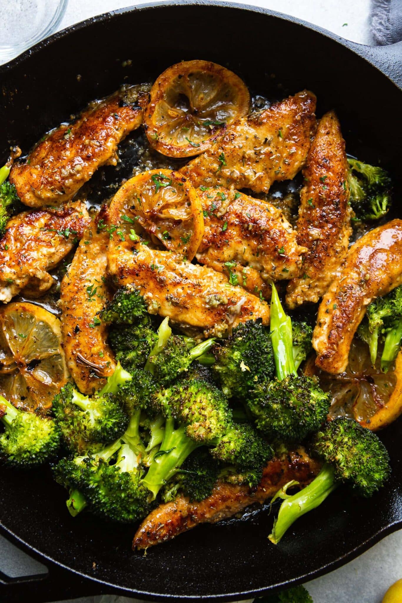 Chicken and broccoli in a skillet with lemon slices.