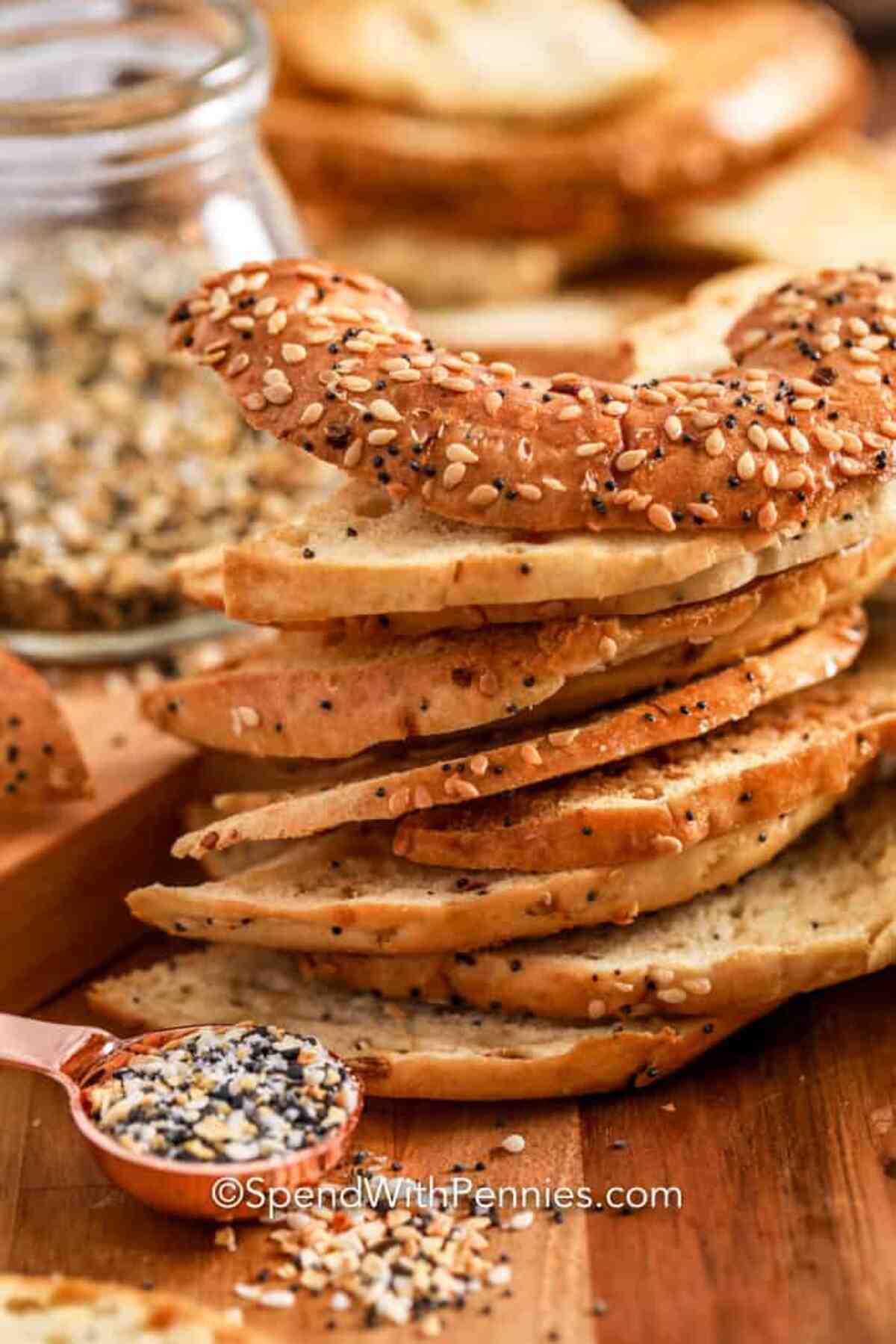 A stack of bagels with sesame seeds on a wooden cutting board.