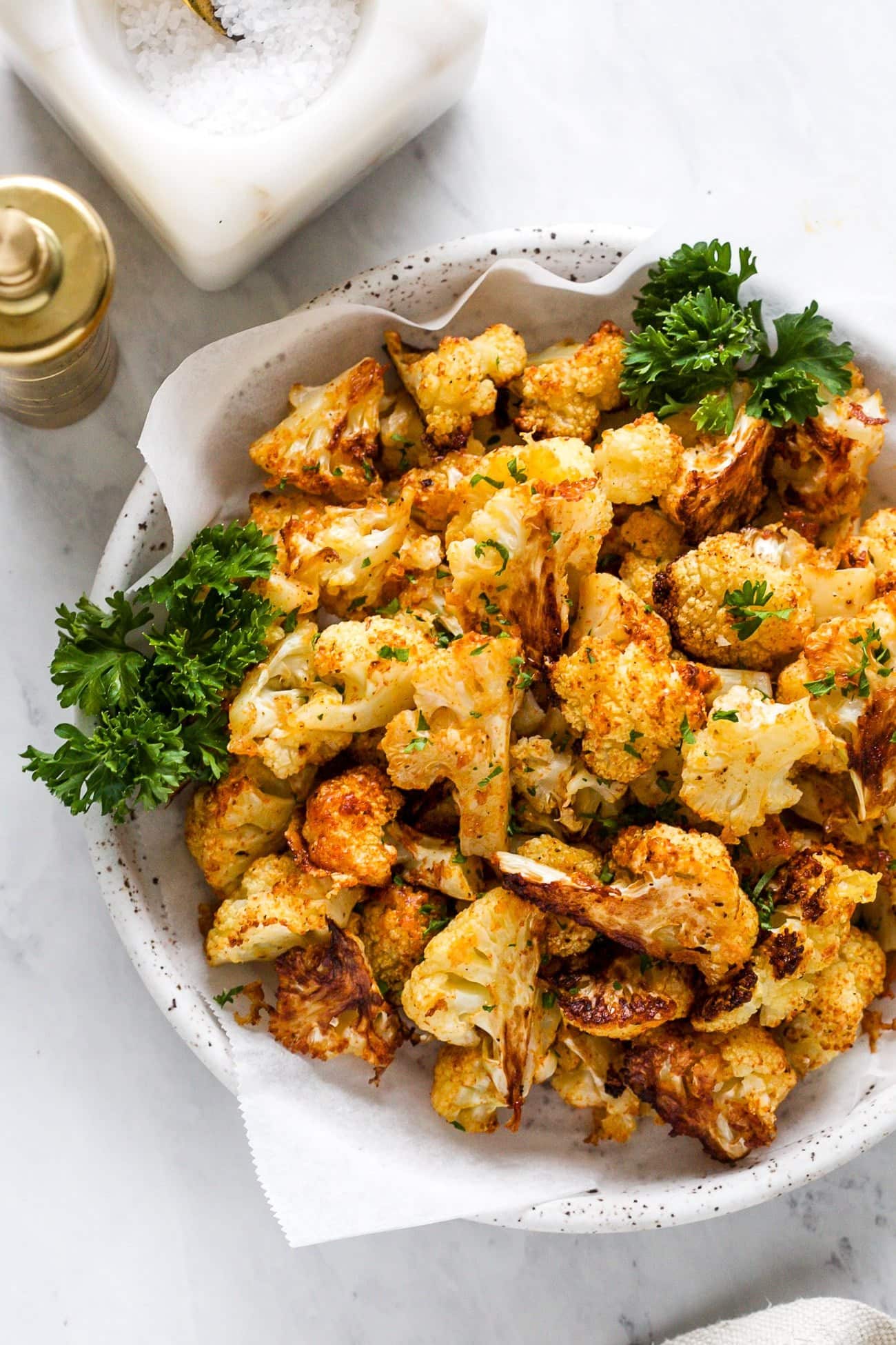 Roasted cauliflower in a white bowl with parsley.