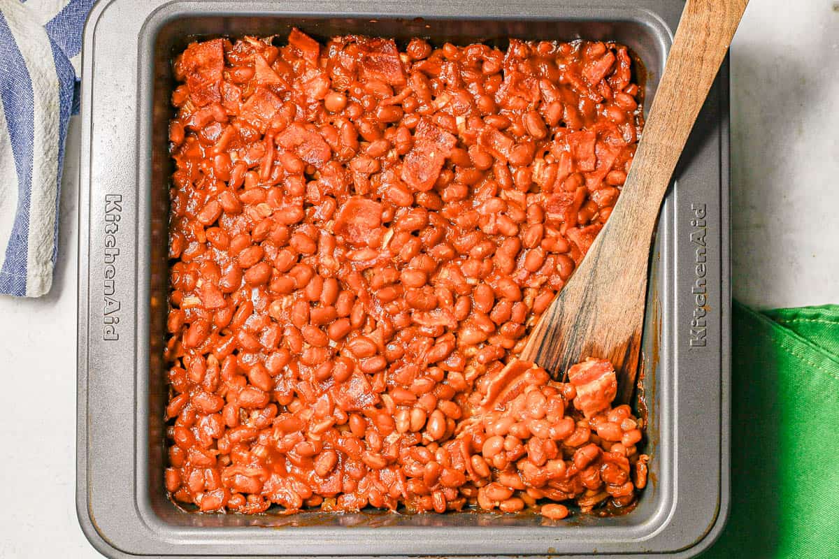 Baked beans in a baking pan with a wooden spoon.