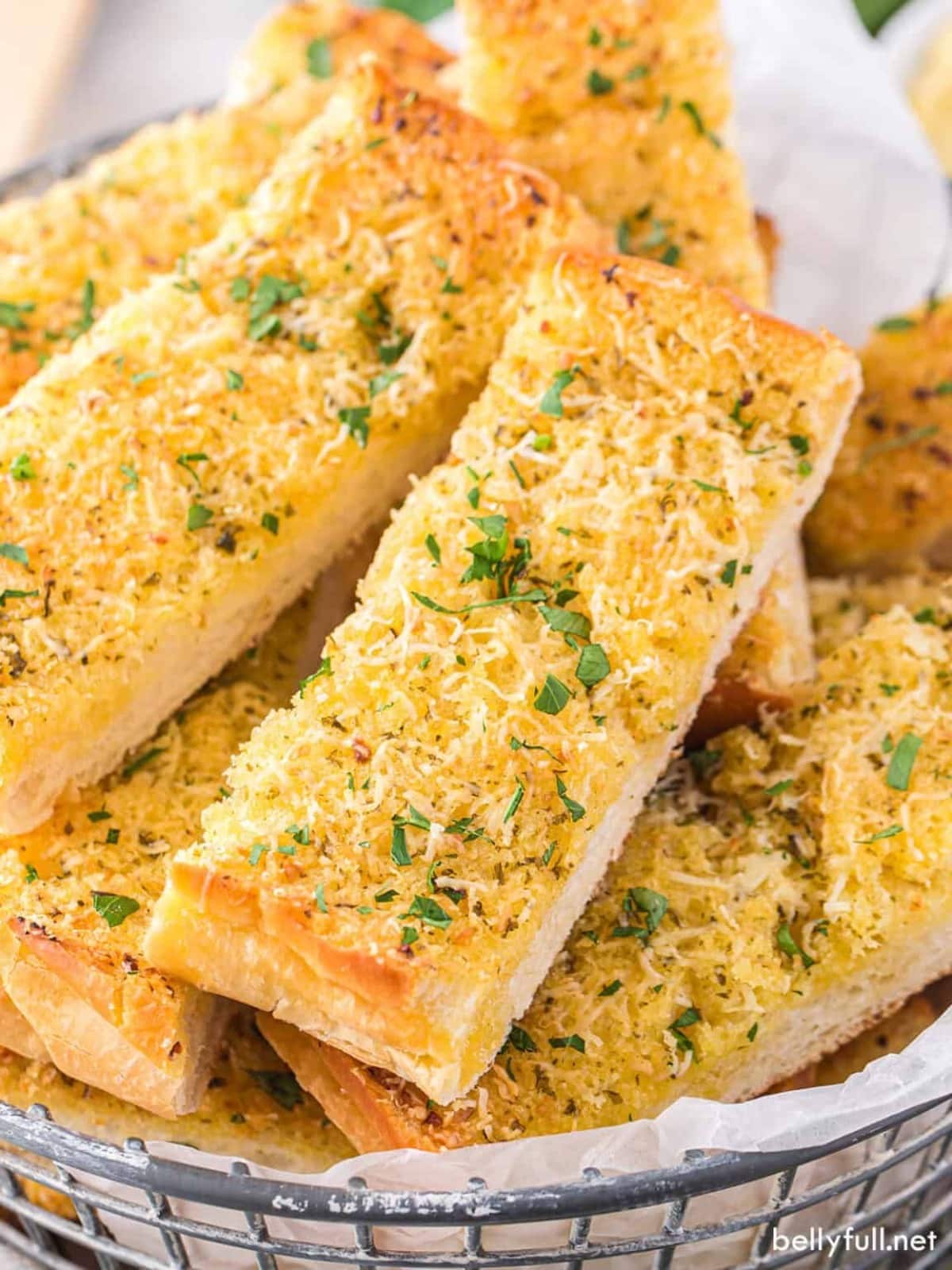 Cheesy bread sticks in a basket with parmesan cheese.