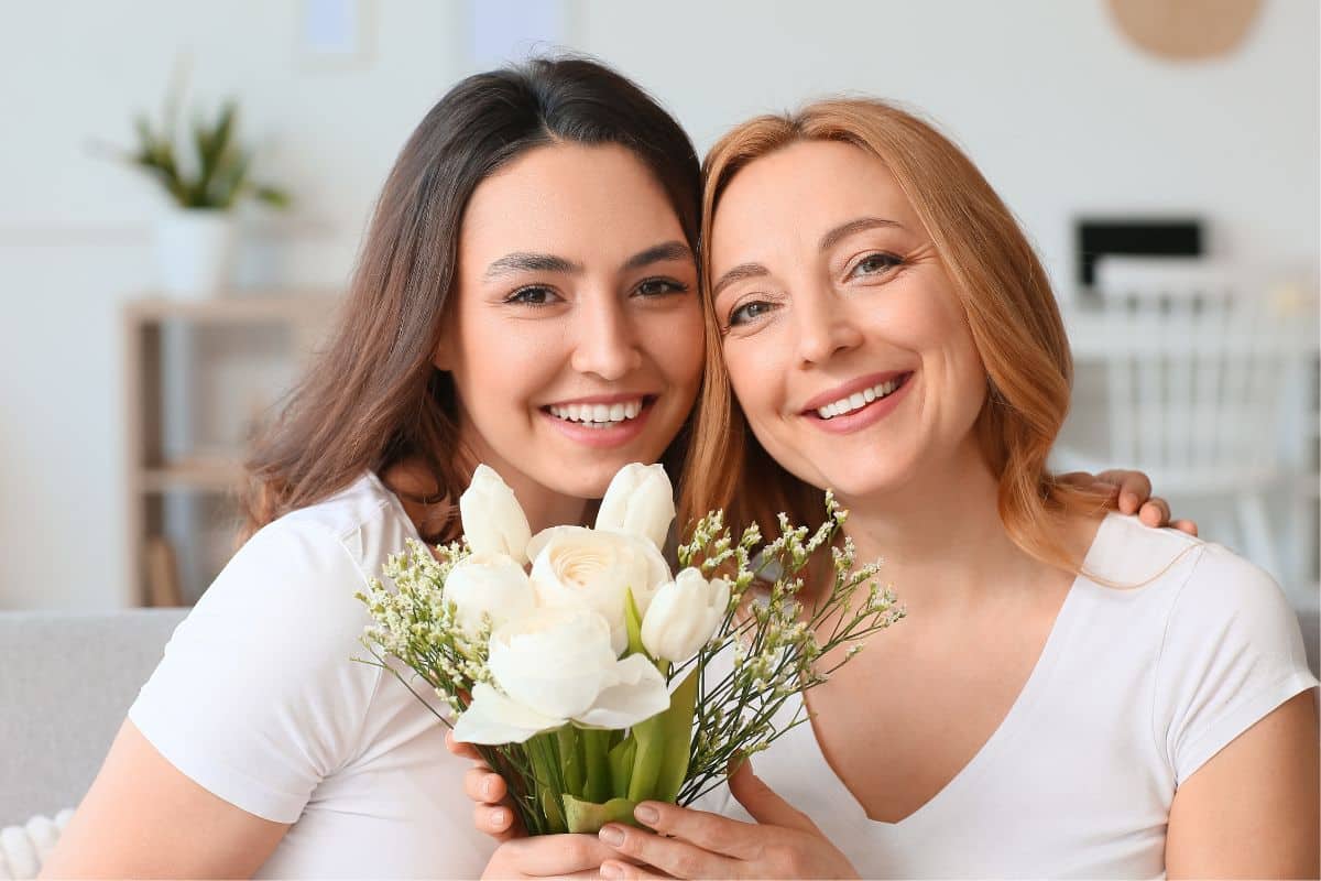 Mother and daughter holding bouquets of flowers on a couch to celebrate a special occasion together.
