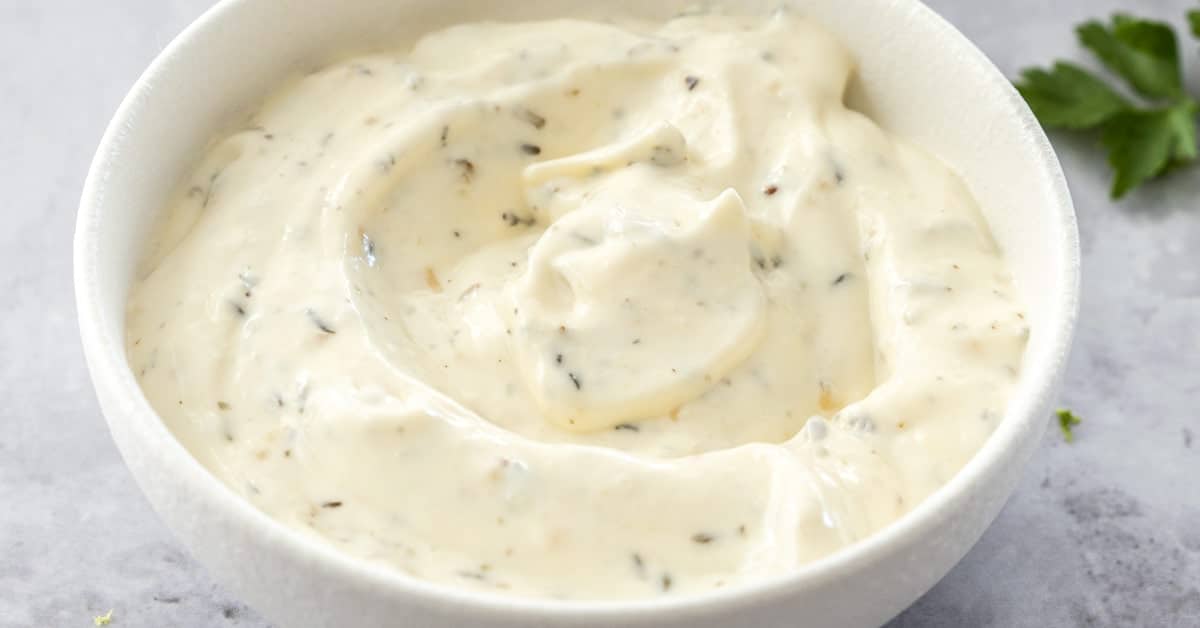 A white bowl with a white sauce and parsley.