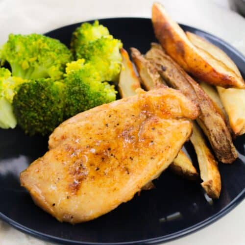 Hot Honey Grilled Chicken Breast with steamed broccoli and baked potato wedges on a black plate.