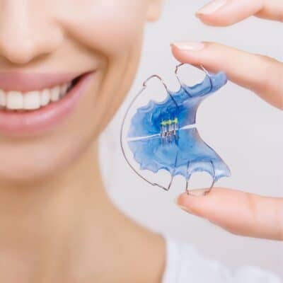 A woman is using a blue tooth whitening device to clean retainers.
