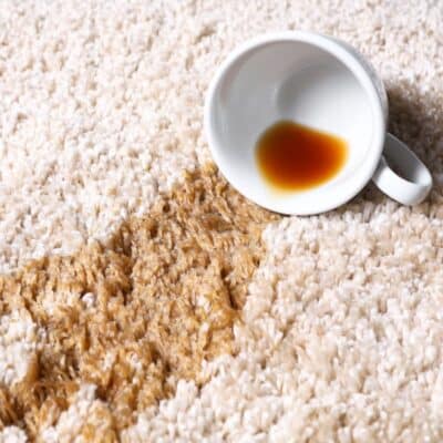 A cup of coffee spilled on a carpet. Learn how to remove tea stains from carpet with these easy tips and tricks.