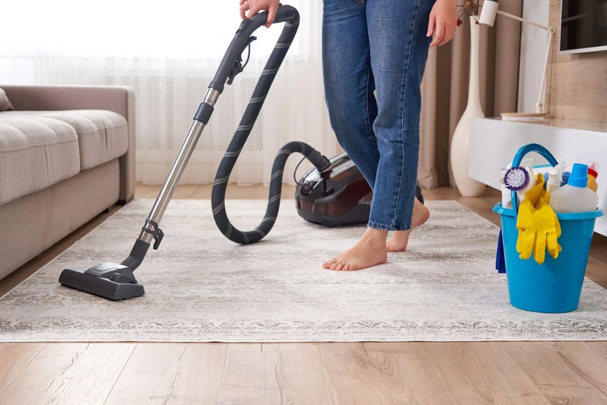 A woman efficiently using a vacuum to remove tea stains from a living room carpet.