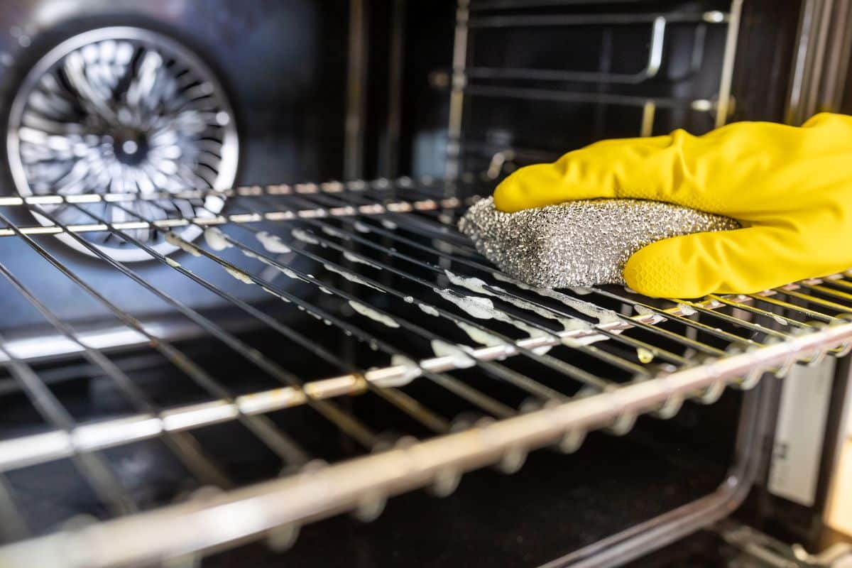 A man with yellow gloves scrubbing the oven racks.