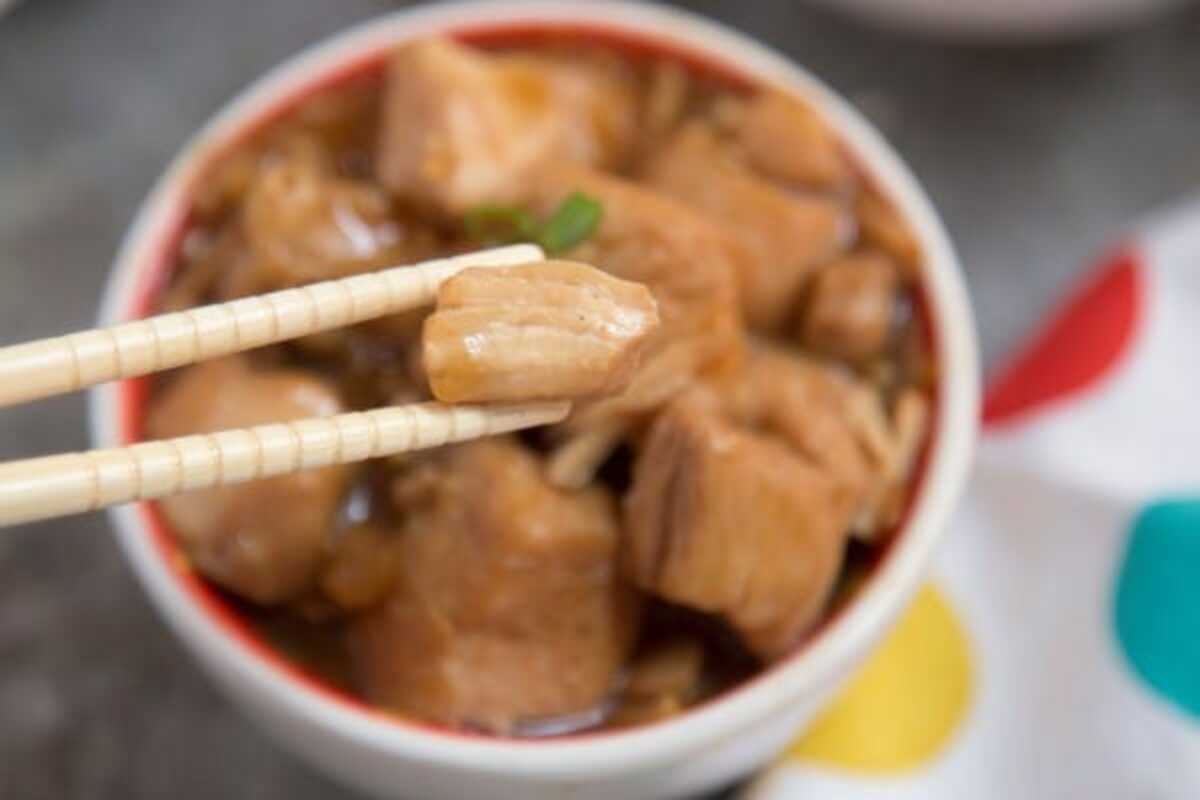 A bowl of chicken with chopsticks in it.