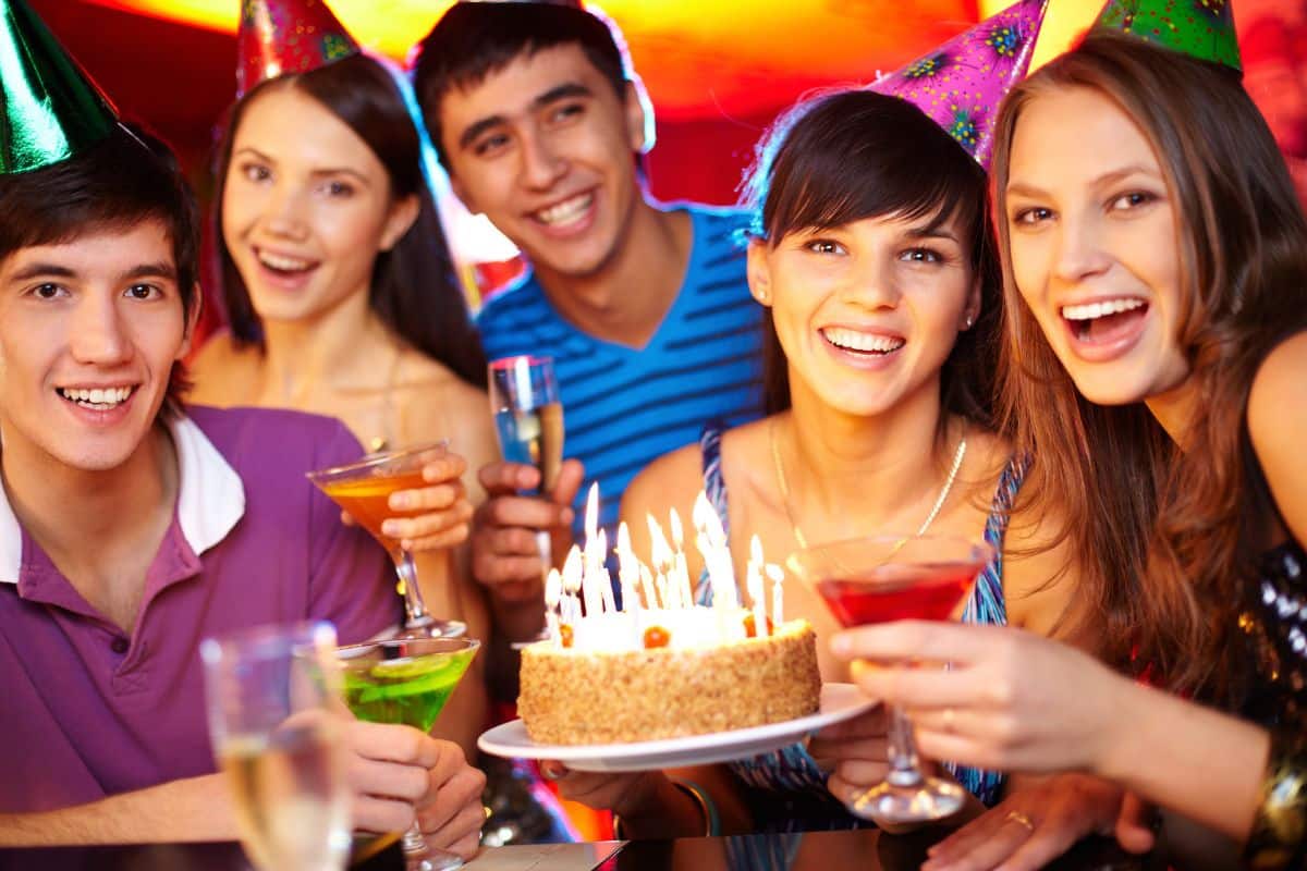 A group of people celebrating with a birthday cake at a teen party.