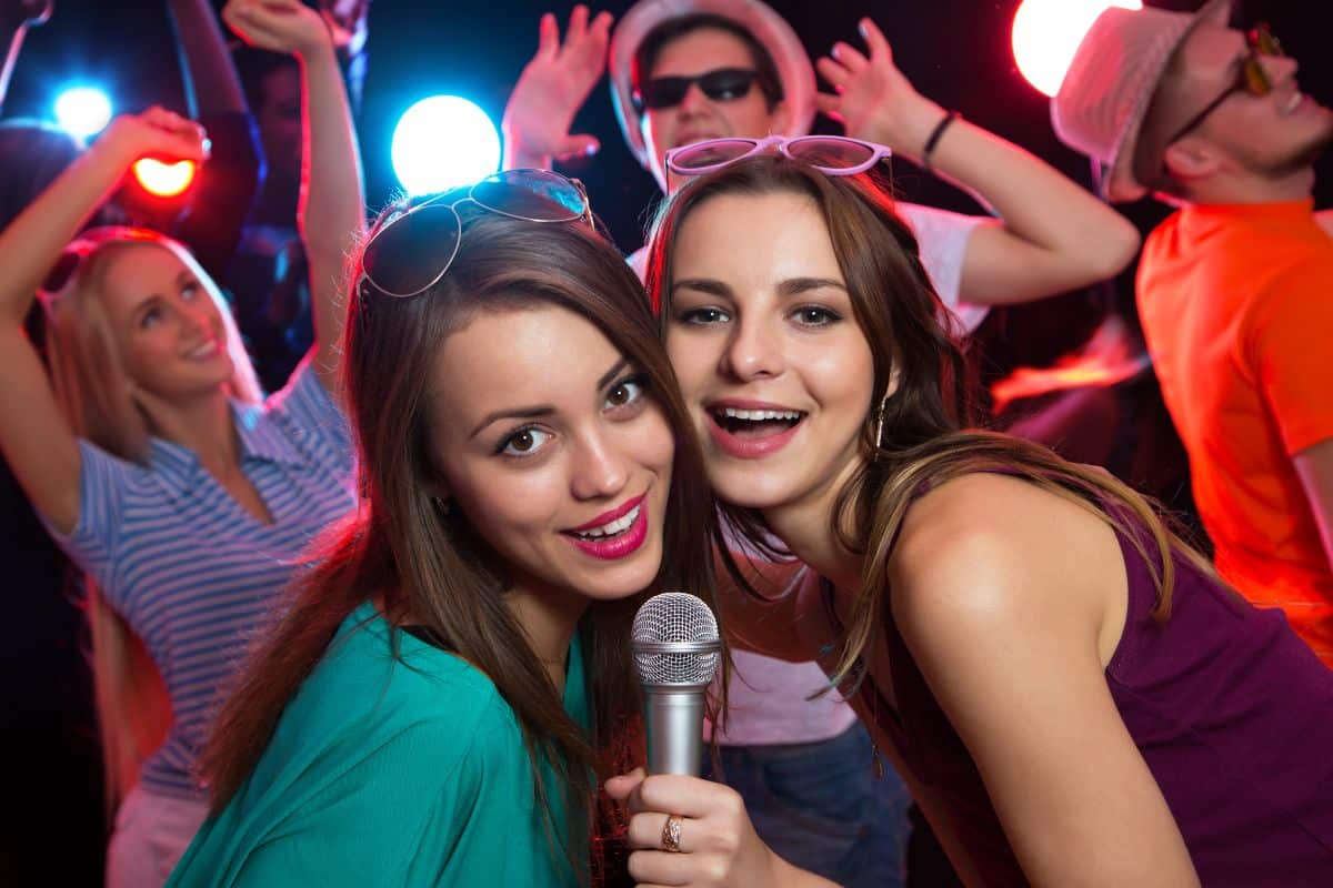 Two teenage girls holding a microphone at a party, adding flair to your teen's party theme ideas.
