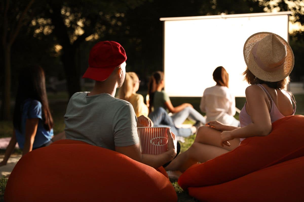 A group of teens sitting in a backyard watching a movie at a party.