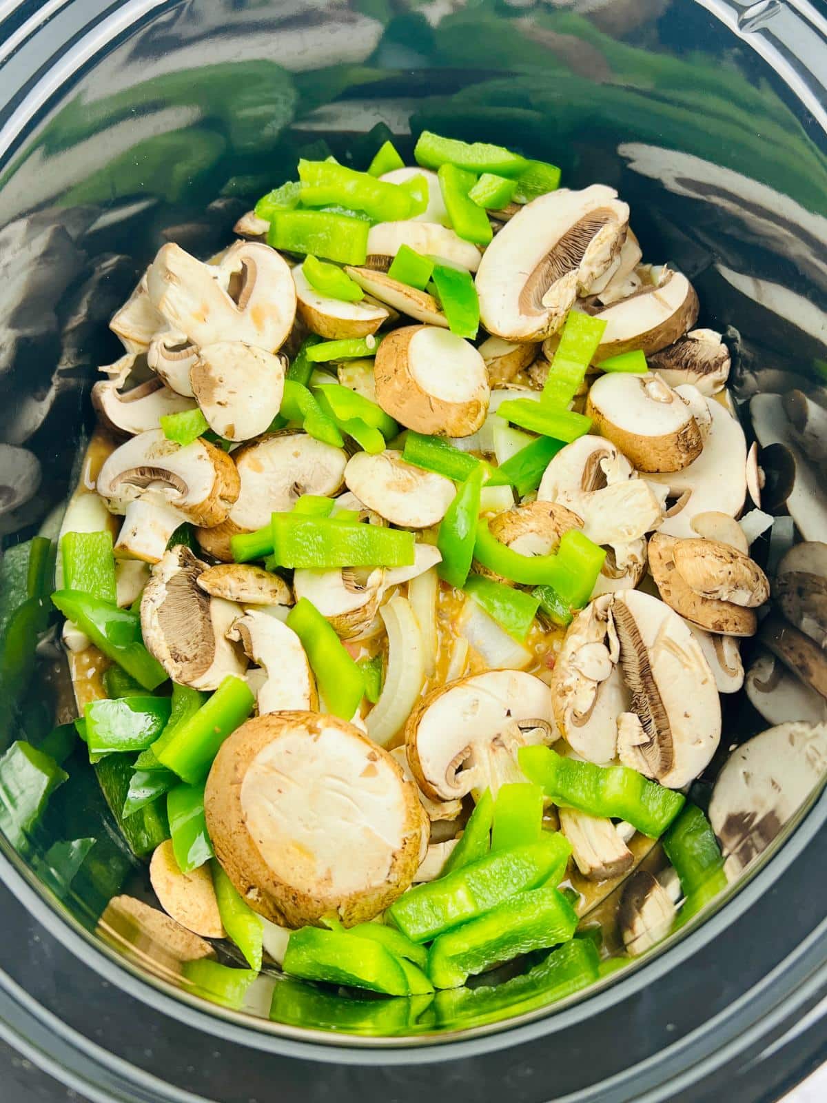 Mushrooms, onions and green bell peppers are added into a Slow Cooker.