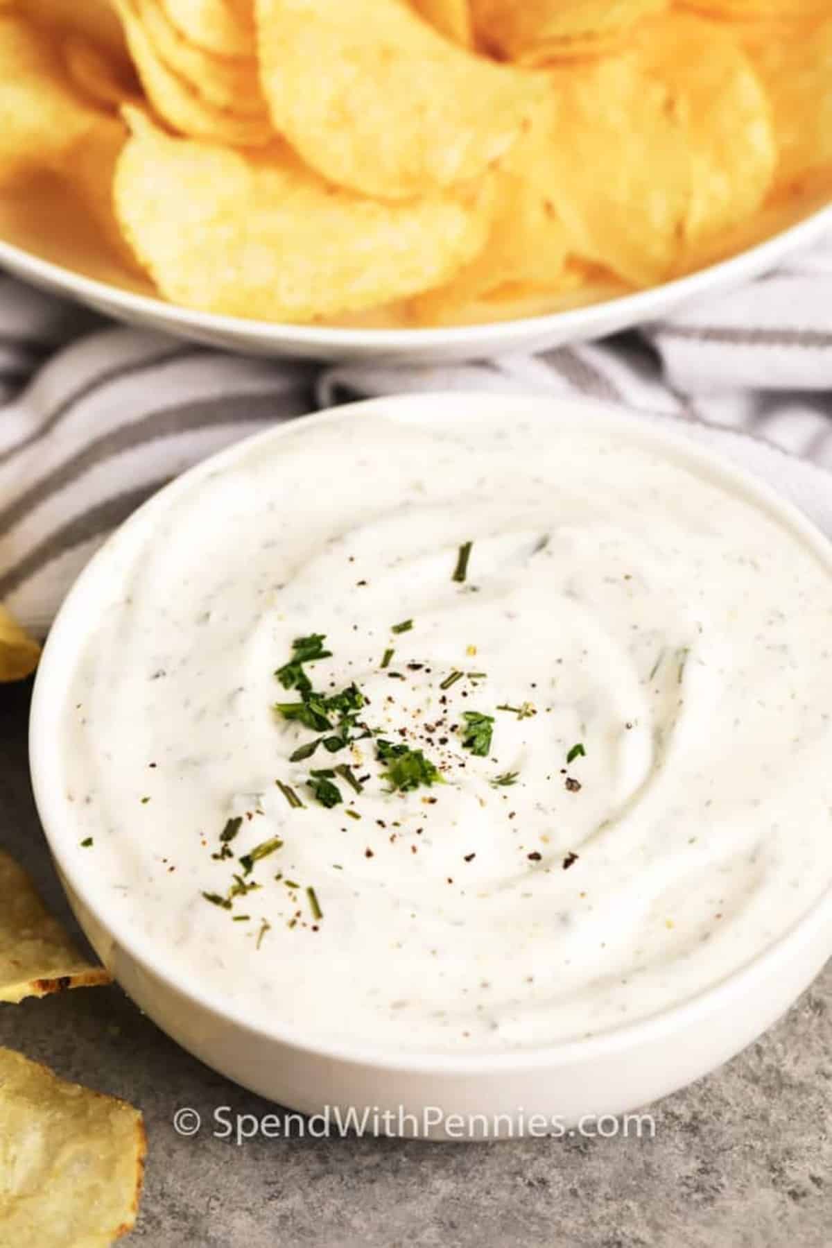 A bowl of dip with chips and herbs.
