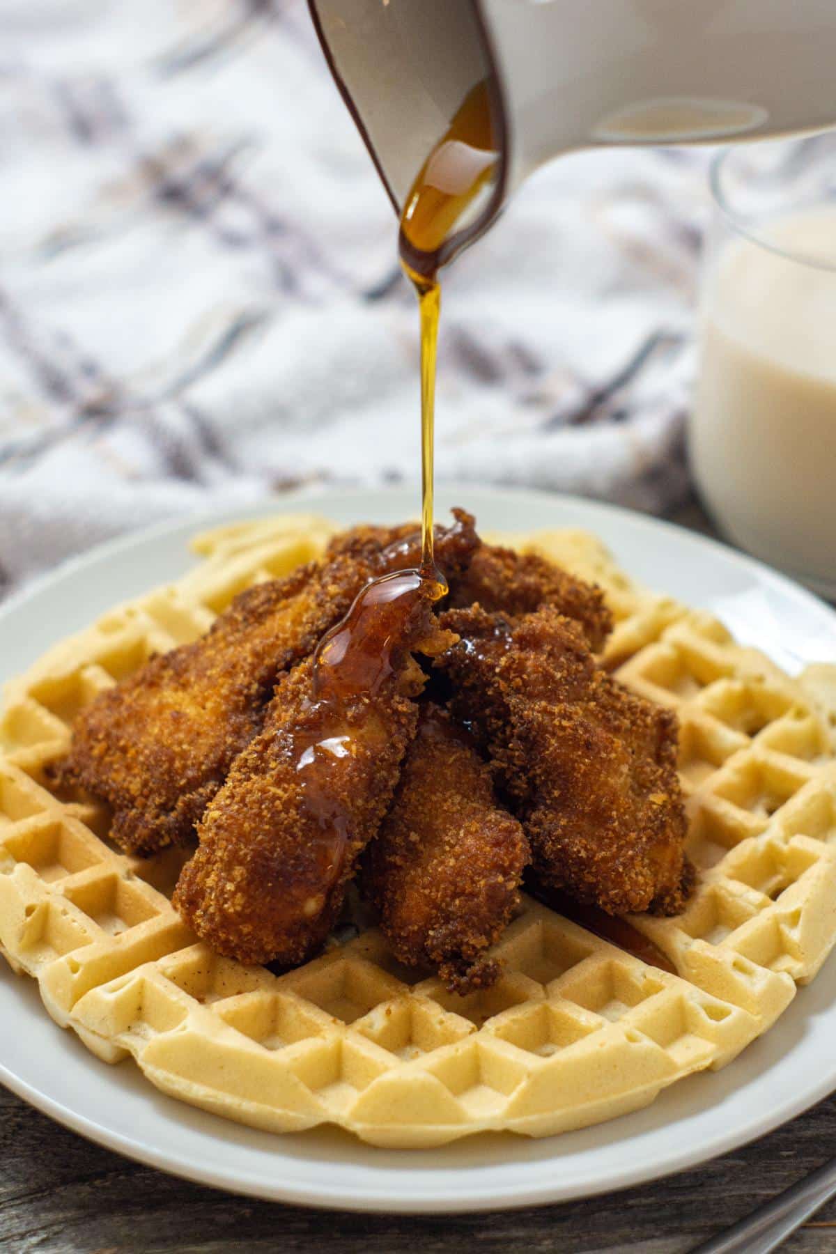Southern chicken and waffles with maple syrup being poured onto a plate.